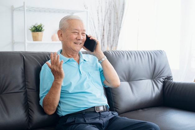 Fröhlicher älterer Mann, der lächelt, während er Smartphone auf Couch zu Hause beantwortet. Glückliches Ruhestandsleben