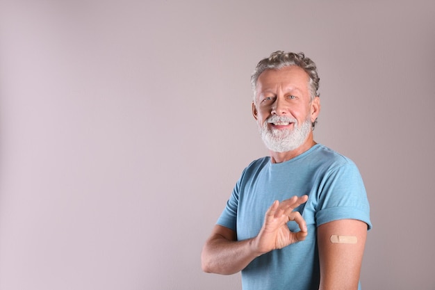 Fröhlicher älterer Mann, der nach der Impfung auf beigem Hintergrund Arm mit Verband zeigt Platz für Text
