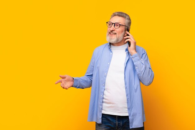 Foto fröhlicher älterer mann spricht am handy auf gelben hintergrund