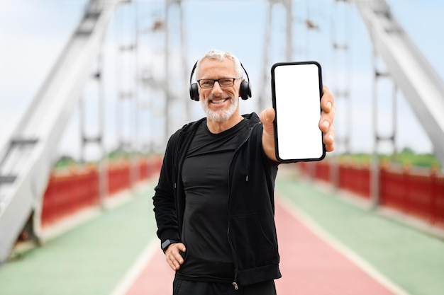 Fröhlicher älterer Sportler zeigt Telefon mit weißem, leerem Bildschirm