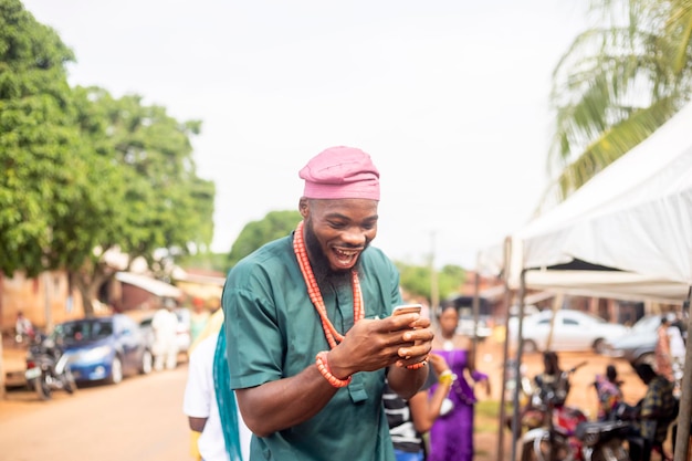 Fröhlicher afrikanischer Mann in traditioneller Kleidung, der lächelnd ein Handy hält