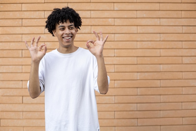 Fröhlicher Afroamerikaner mit lockigem Haar, der mit beiden Händen ok zeigt und wegschaut