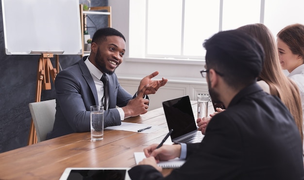 Fröhlicher afroamerikanischer Bewerber, der beim Vorstellungsgespräch mit der HR-Kommission spricht