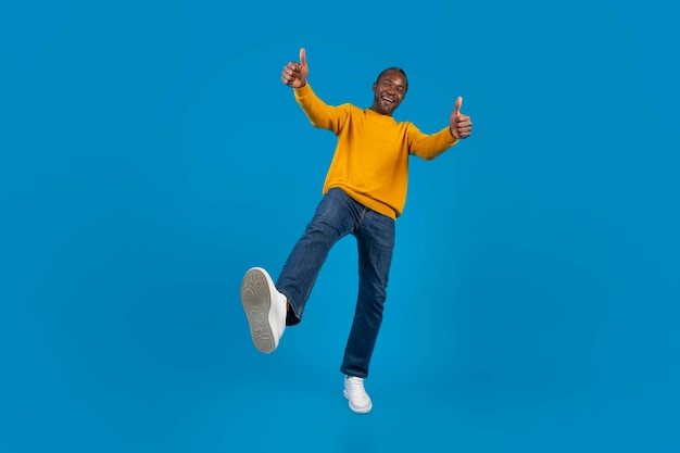 Fröhlicher afroamerikanischer Mann, der Daumen hoch auf Blau zeigt
