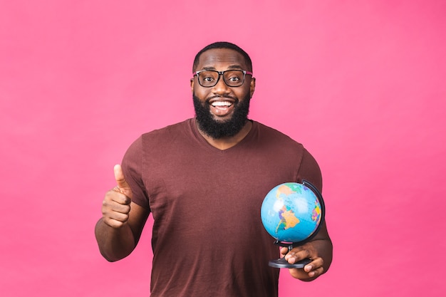 Fröhlicher afroamerikanischer schwarzer Mann, der den Globus mit Liebe und Sorgfalt einzeln auf rosafarbenem Hintergrund hält. Reisekonzept, auf der Suche nach einer Reise.