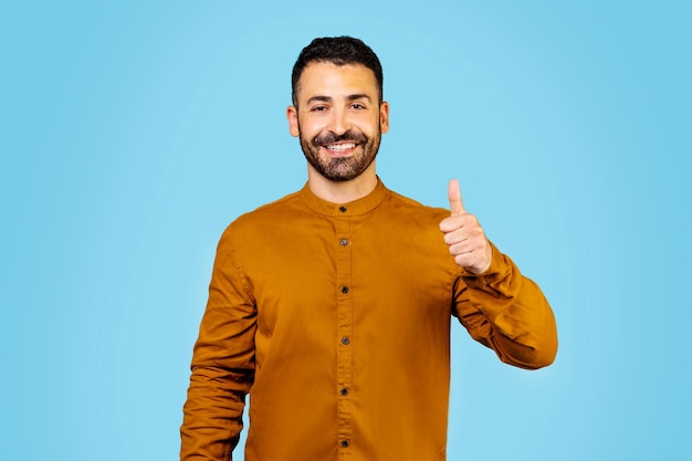 Fröhlicher arabischer Mann, der mit dem Finger auf die Klasse zeigt, während er in die Kamera lächelt und vor blauem Hintergrund steht