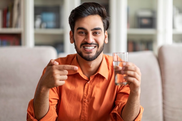 Fröhlicher arabischer Typ, der auf ein Glas Wasser nach Hause zeigt