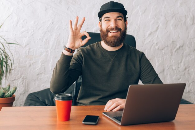 Fröhlicher Arbeiter, der im Büro sitzt und OK-Geste zeigt