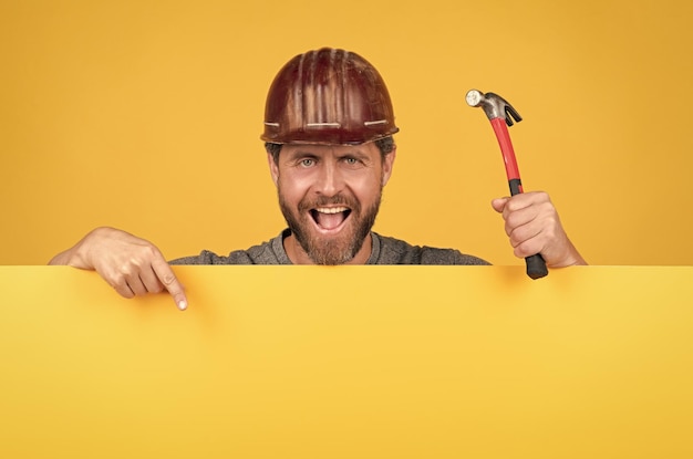 Fröhlicher Arbeitstag reifer Mann im Helm mit Hammerbauer zeigt Finger auf Kopierraum