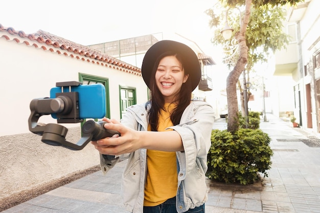 Fröhlicher asiatischer Influencer, der Spaß beim Vlogging mit Gimbal und Handy im Freien hat - Fokus auf Gesicht
