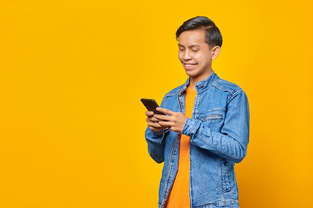 Fröhlicher asiatischer Mann mit Smartphone auf gelbem Hintergrund