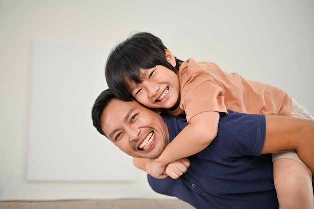Fröhlicher asiatischer Sohn und Vater, die sich zu Hause beim Spielen und Huckepack vergnügen