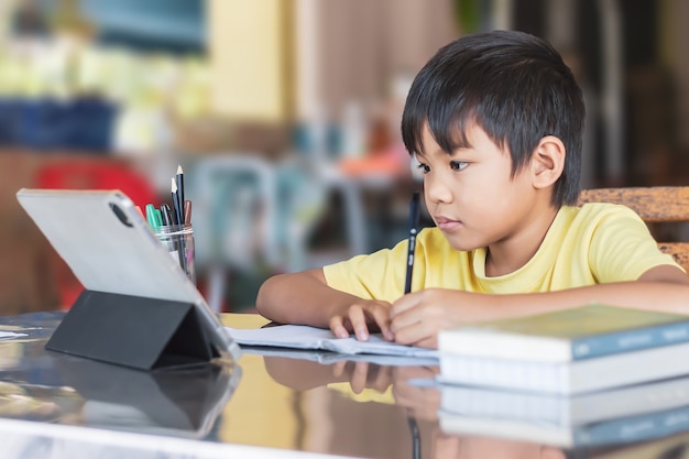 Foto fröhlicher asiatischer studentenjunge, der smart pad oder tablet für seine hausaufgaben verwendet und berührt