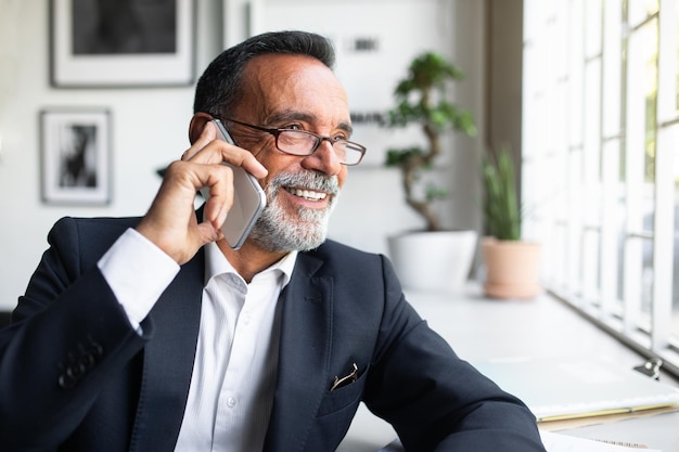 Fröhlicher, attraktiver kaukasischer alter Geschäftsmann in Anzug und Brille, der per Smartphone anruft