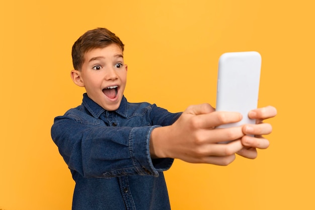 Fröhlicher, aufgeregter Teenager schaut schockiert auf den Smartphone-Bildschirm