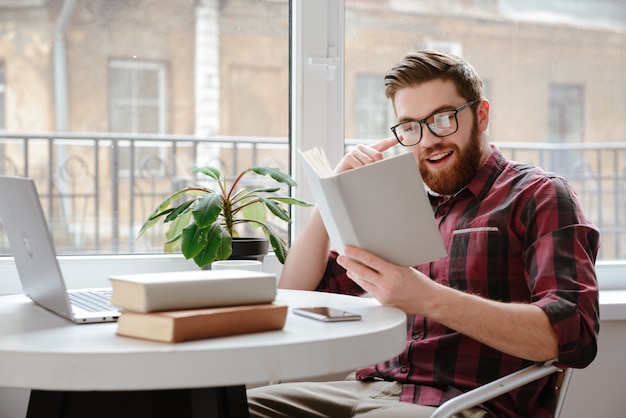 Fröhlicher bärtiger junger Mann, der Bücher liest.