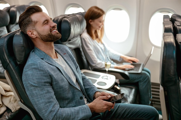 Fröhlicher bärtiger Mann mit Smartphone, der mit dem Flugzeug reist