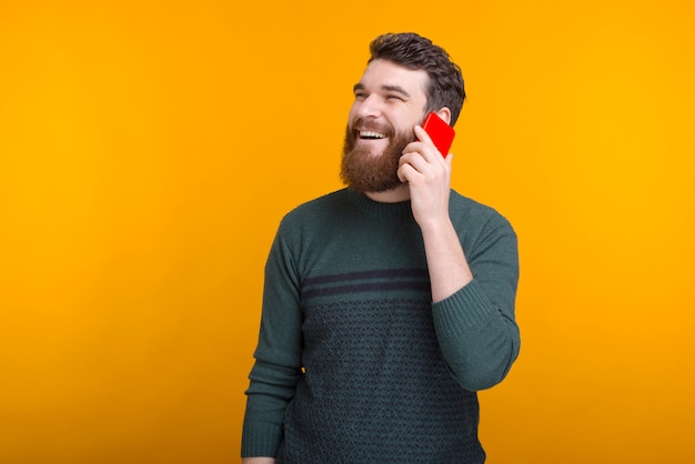 Fröhlicher bärtiger Mann spricht am Telefon und lächelt auf gelbem Raum.