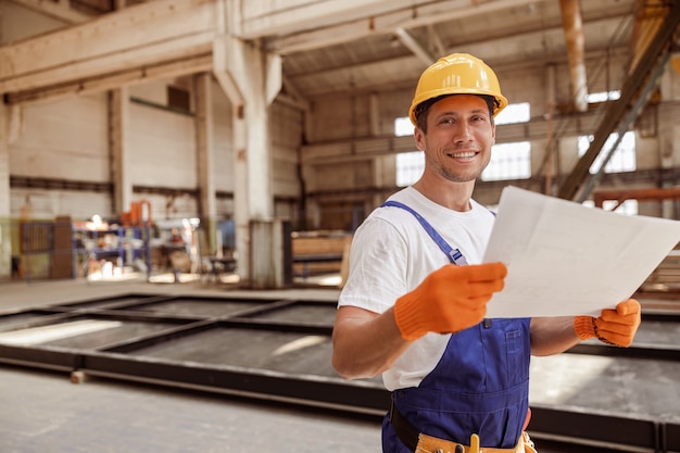 Fröhlicher Baumeister, der den Architekturplan auf der Baustelle studiert