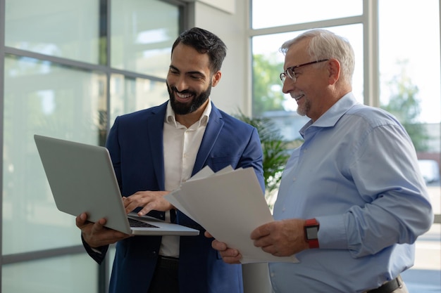 Fröhlicher brünetter Büroangestellter, der Laptop hält, während er sein Startup präsentiert