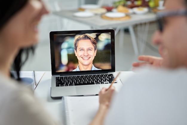 Fröhlicher Eheberater, der seine Kunden anlächelt, eine Video-Chat-App verwendet und während der Sperrung Hilfe leistet. Online-Beratungskonzept. Fokus auf Laptop-Bildschirm