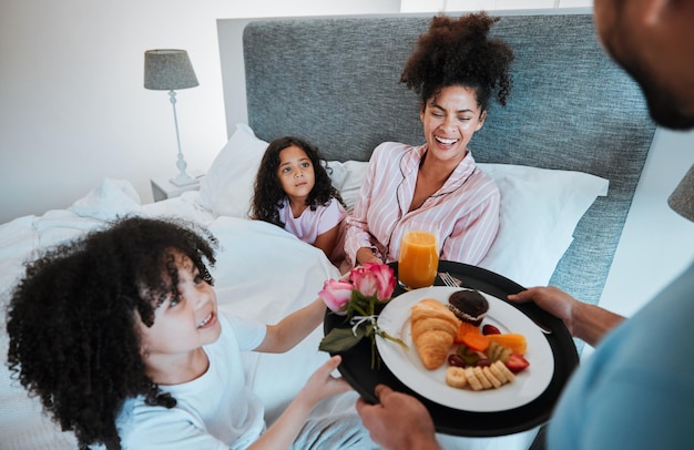 Fröhlicher Familienmuttertag und morgendliches Frühstück im Bett zum Feiern der Liebe und gemeinsamen Fürsorge zu Hause. Vater und Kinder geben der Mutter Essen, Essen oder ein Geschenk für den Start in den Urlaub oder das Wochenende im Schlafzimmer