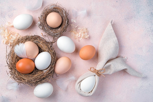 Fröhlicher festlicher Osterhintergrund mit natürlichen Eiern im Nest und einem Osterhasen aus einer Serviette auf einem hellrosa Hintergrund