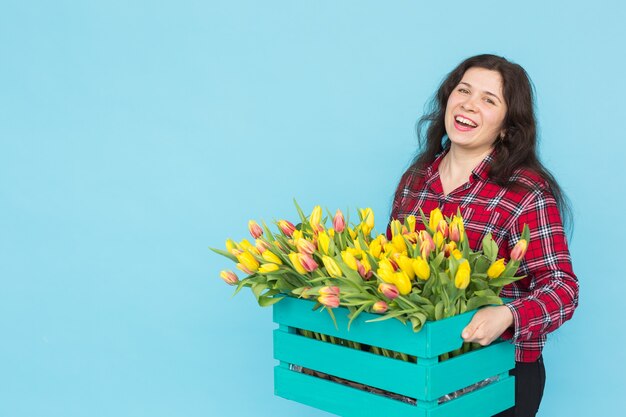 Fröhlicher Florist der jungen Frau mit Schachtel Tulpen über blauer Oberfläche mit Kopienraum