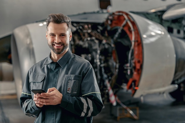 Fröhlicher Flugmechaniker mit Handy im Hangar