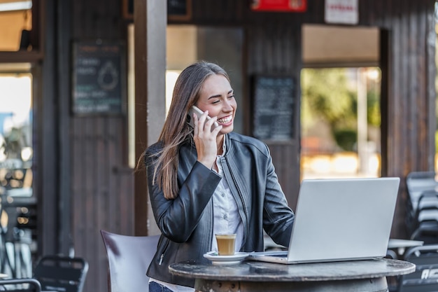 Fröhlicher Freelancer spricht über sein Smartphone in einer Außencafeteria