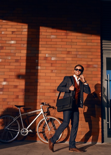 Fröhlicher Geschäftsmann, der auf Smartphone nahe Fahrrad spricht