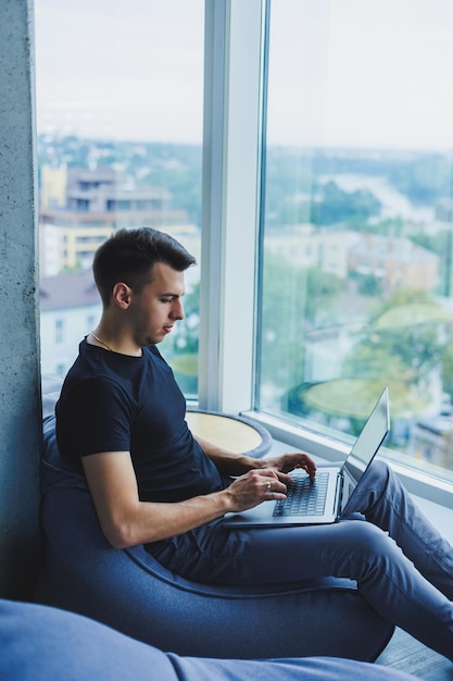 Fröhlicher Geschäftsmann sitzt und arbeitet mit einem Laptop im Büro Ein Geschäftsmann sitzt und arbeitet an einem Laptop-Computer Den Tag im Büro beginnen