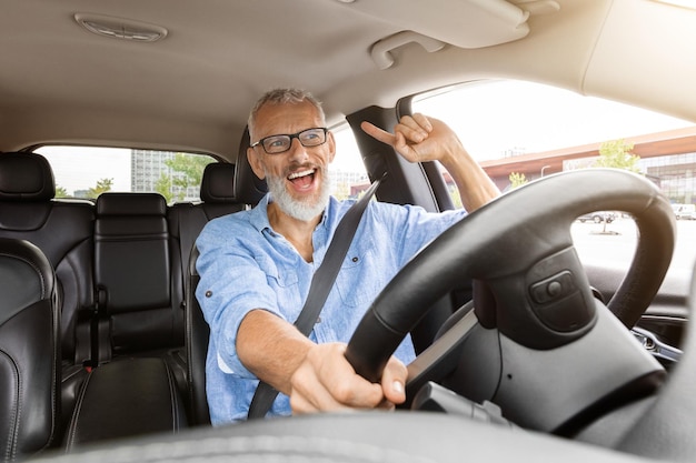 Fröhlicher, gutaussehender älterer Mann, der in seinem neuen Auto Musik hört