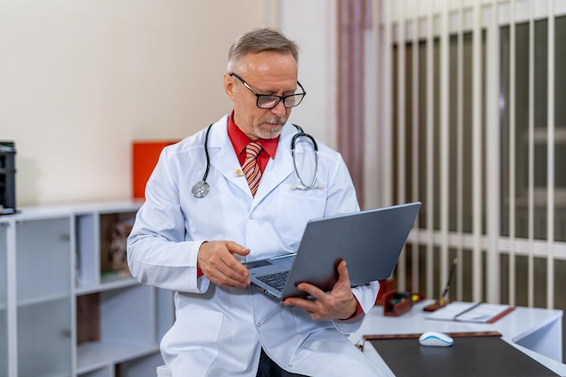 Fröhlicher, gutaussehender Arzt, der mit dem Computer arbeitet. Stilvoller Mediziner mit Brille.