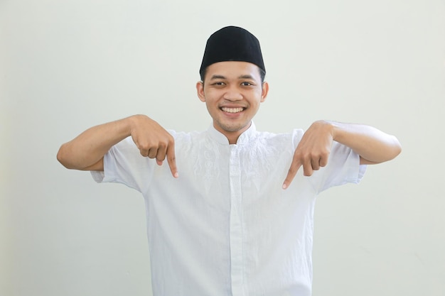 Fröhlicher, gutaussehender junger asiatischer muslimischer Mann mit arabischem Kostüm, der mit dem Finger auf den freien Platz zeigt