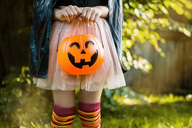 Fröhlicher Halloween-Tag Ein kleines Kind in einem Hexenkostüm sucht nach Süßigkeiten in seinem Kürbis-Jack-Eimer