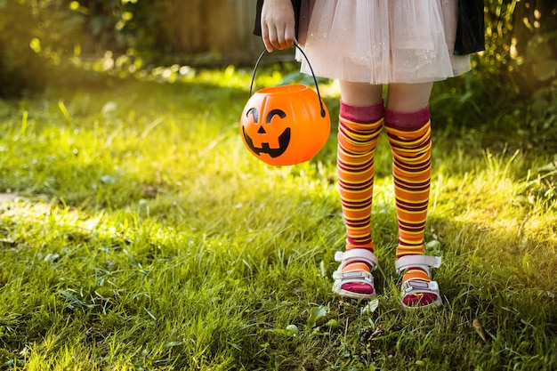 Fröhlicher Halloween-Tag Ein kleines Kind in einem Hexenkostüm sucht nach Süßigkeiten in seinem Kürbis-Jack-Eimer