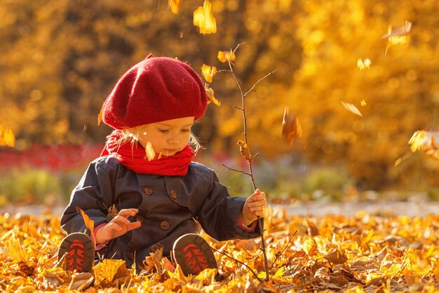 Fröhlicher Herbst Ein kleines Mädchen in einer roten Baskenmütze spielt mit fallenden Blättern und lacht