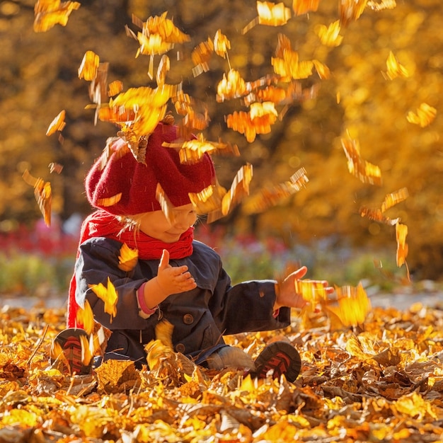 Fröhlicher Herbst Ein kleines Mädchen in einer roten Baskenmütze spielt mit fallenden Blättern und lacht