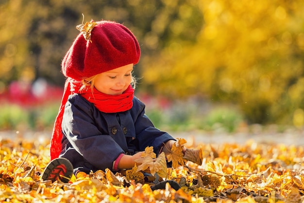 Fröhlicher Herbst Ein kleines Mädchen in einer roten Baskenmütze spielt mit fallenden Blättern und lacht