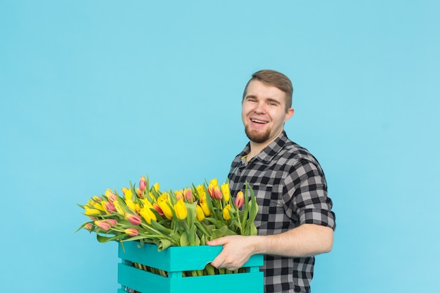 Fröhlicher hübscher Mannflorist, der Schachtel Tulpen auf blauer Wand hält,