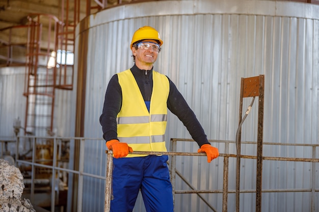 Fröhlicher Ingenieur, der in der Nähe des Meta-Lagerbehälters in der Fabrik steht