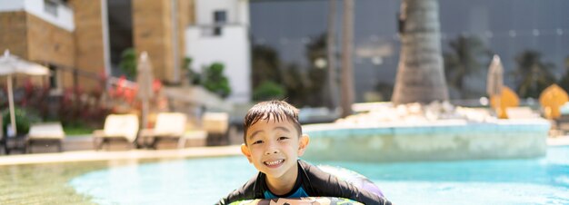 Fröhlicher Junge, der im Schwimmbad spielt, lächelt und in die Kamera schaut, Panorama mit Kopierraum