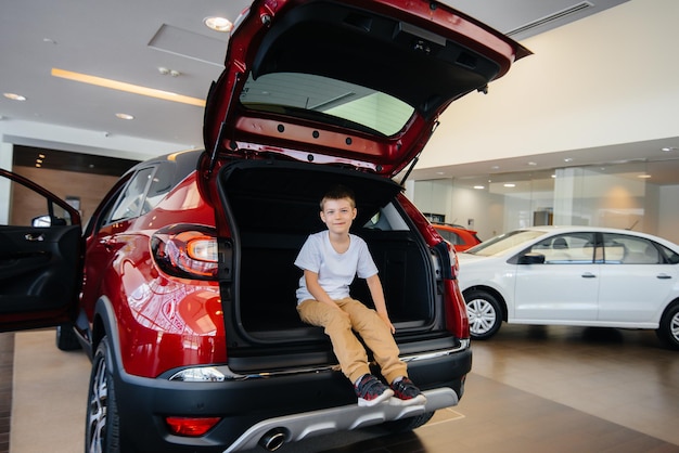 Fröhlicher Junge, der in einem Autohaus im Kofferraum eines neuen Autos sitzt. Ein Auto kaufen.