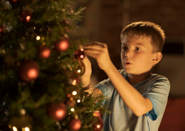 Fröhlicher Junge, der zu Hause seinen Weihnachtsbaum schmückt