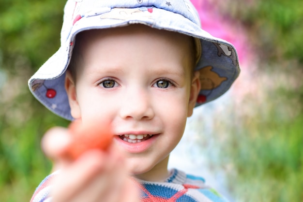 Fröhlicher Junge hält Erdbeeren im Garten