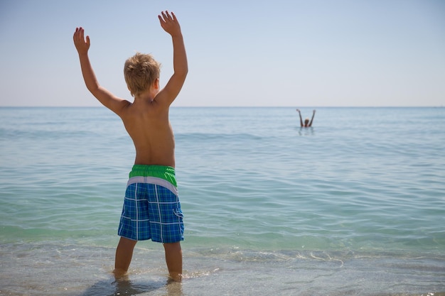 Fröhlicher Junge in Flossen, der an einem sonnigen Tag am Meeresufer steht. Kind wird im Meer schwimmen. Urlaub Aktivitäten für Kinder am Strand Freude und Glück