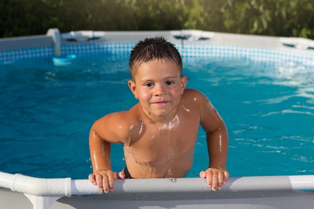 Foto fröhlicher junge klettert aus dem pool und lehnt sich an den rand