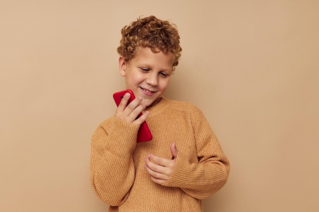 Fröhlicher Junge mit rotem Telefon in Händen, der beigen Hintergrund aufwirft