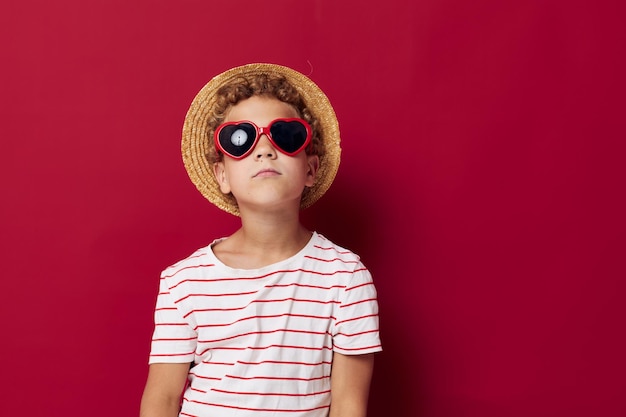 Fröhlicher Junge mit Sonnenbrille posiert auf rotem Hintergrund der Mode